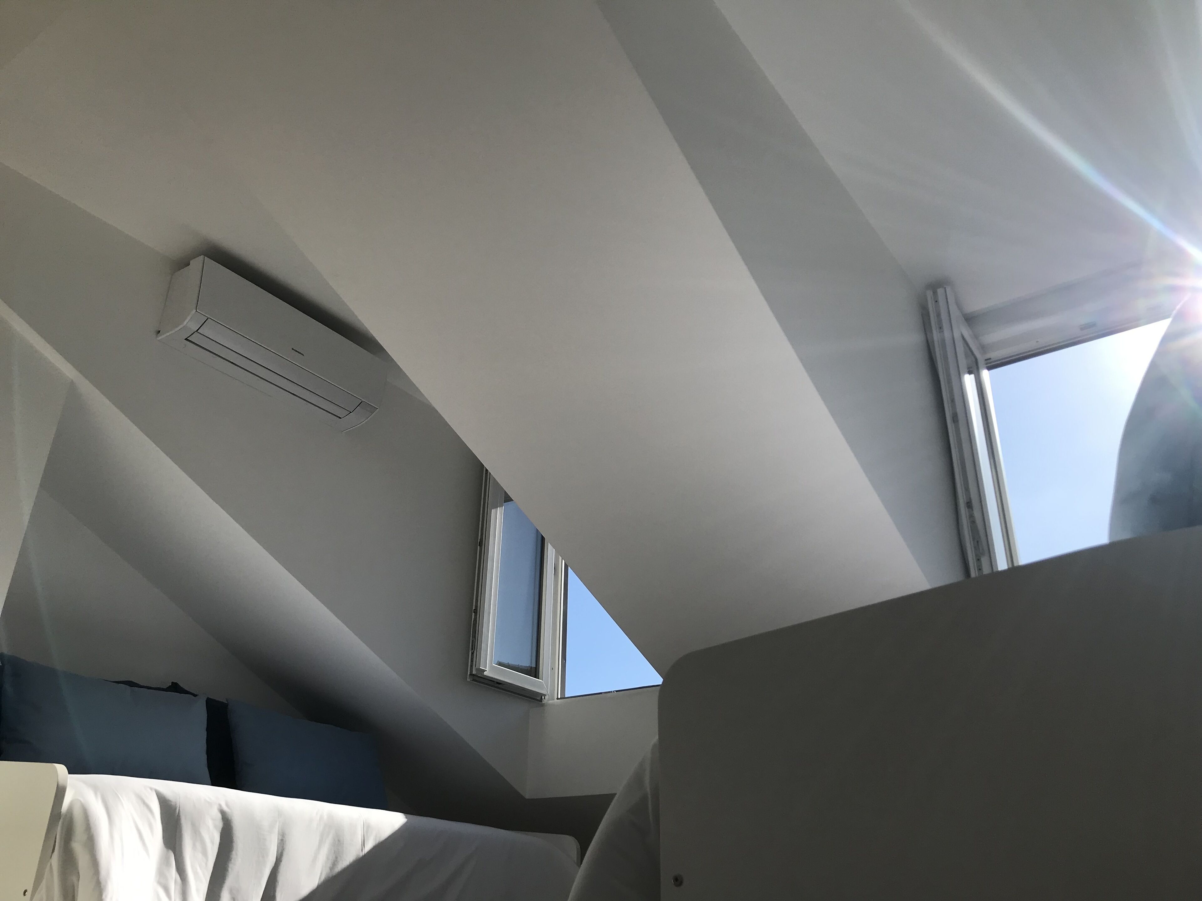 Ein Zimmer mit schrägem Dach, einem Fenster und einer Wand-Klimaanlage.