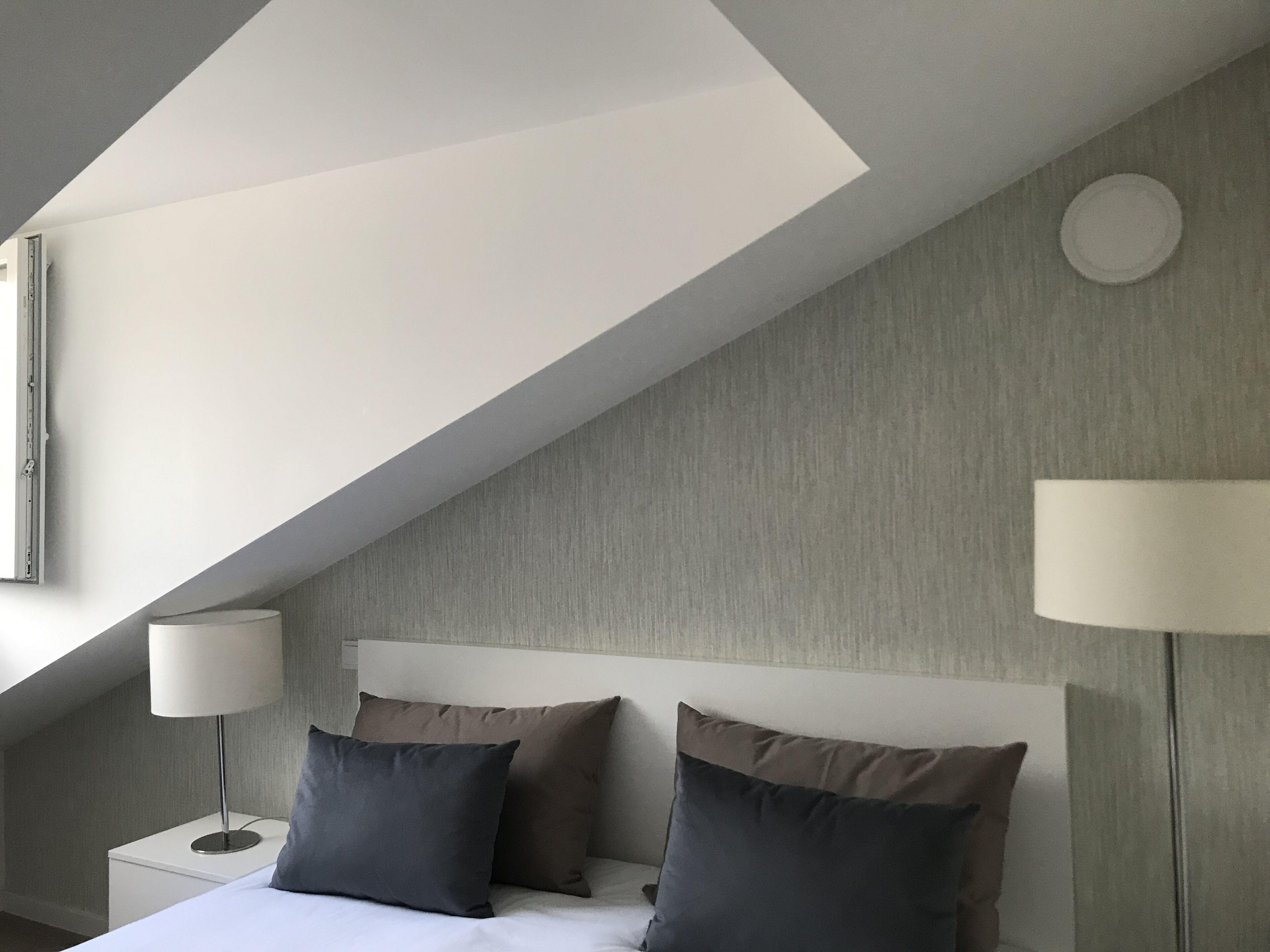 Un dormitorio moderno con techo inclinado, una cama con dos almohadas, una mesita de noche y dos lámparas de noche.