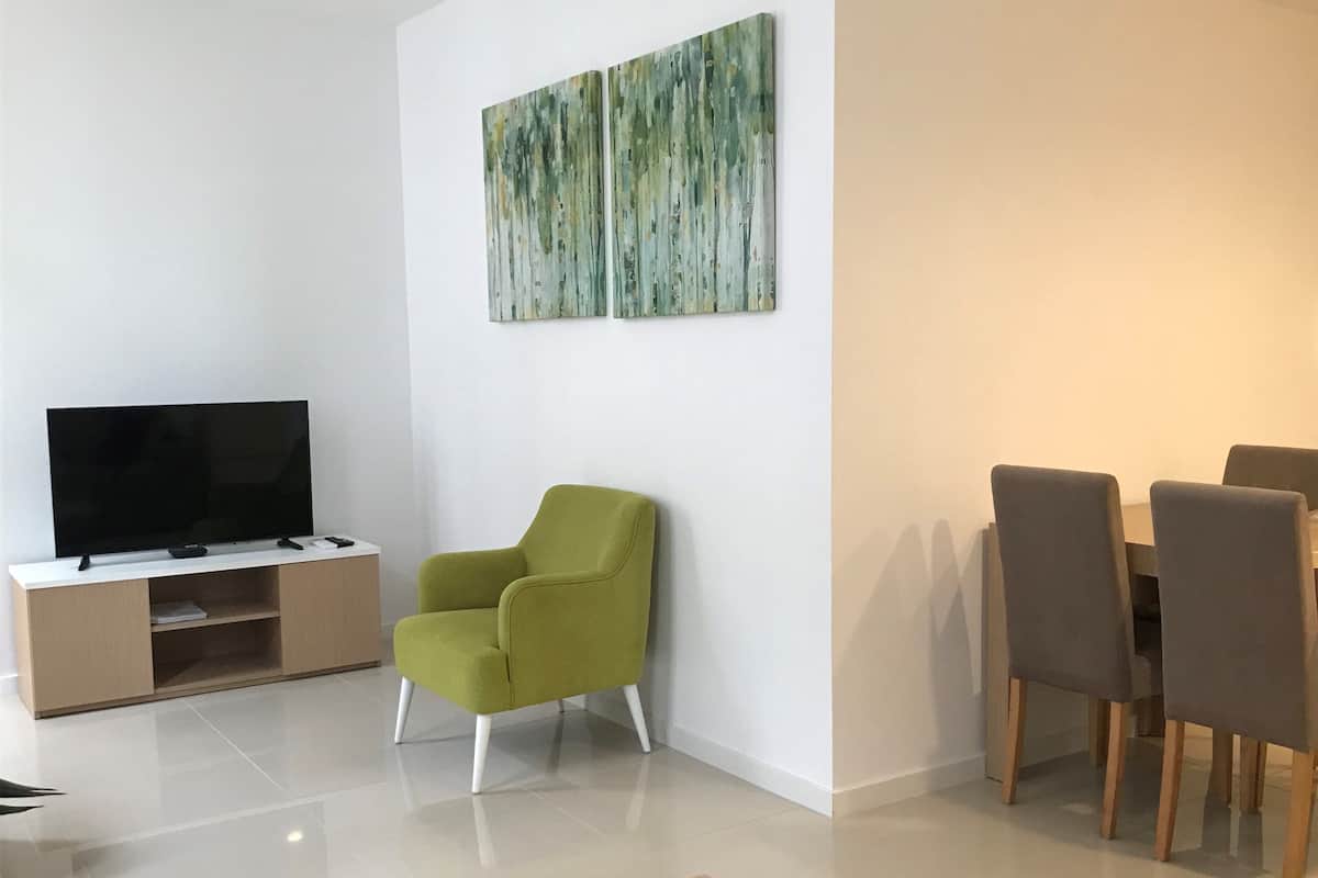 A modern living room with a flat-screen TV, a green armchair, a dining table with chairs, and abstract wall art.