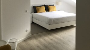 Un dormitorio con cama, mesita de noche, lámpara y un pequeño cubo de basura.