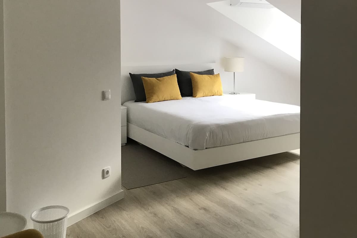 A bedroom with a bed, a nightstand, a lamp, and a small trash bin.