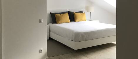 Un dormitorio con cama, mesita de noche, lámpara y un pequeño cubo de basura.