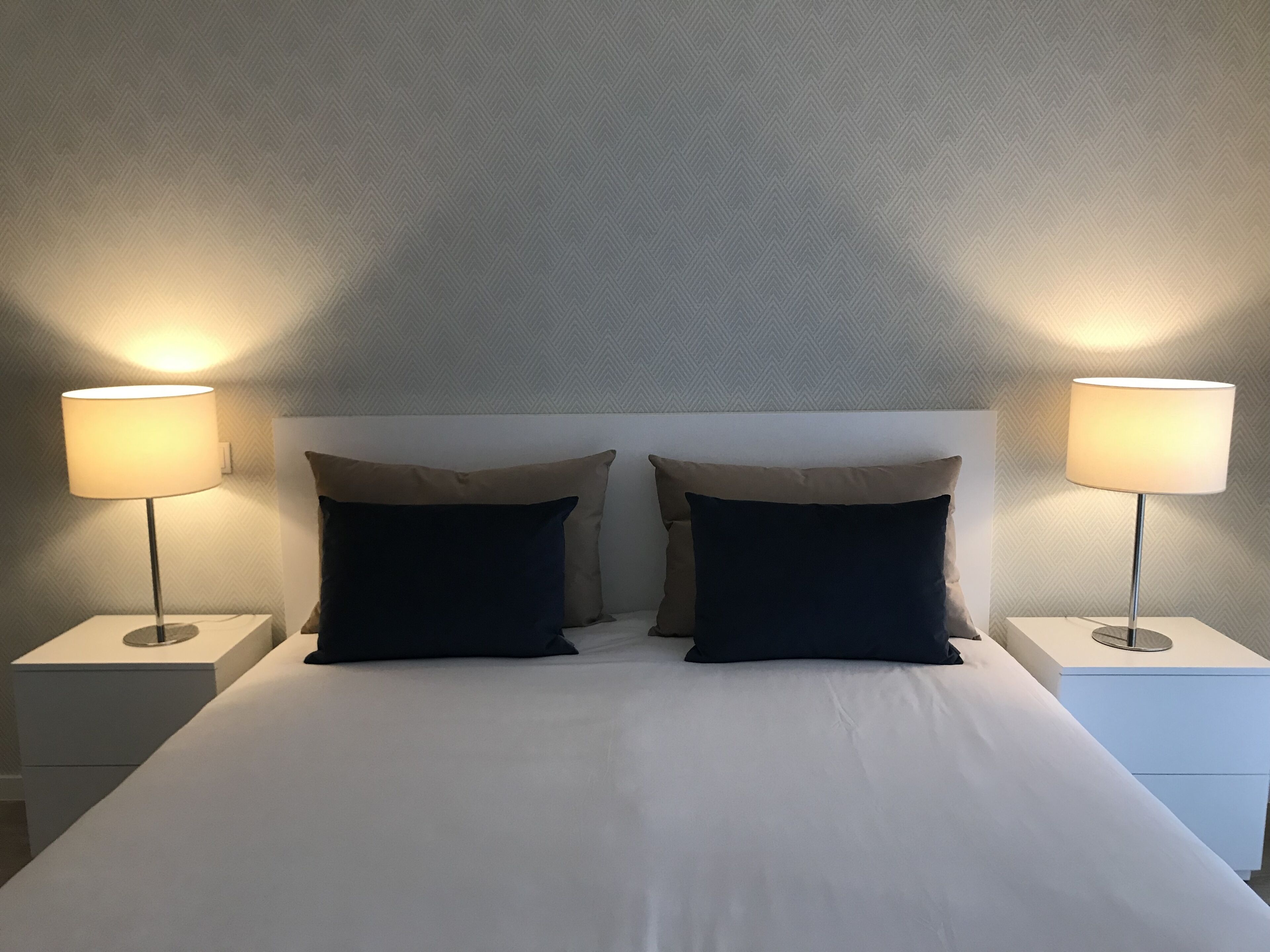 A neatly made bed with two pillows and two bedside lamps on white nightstands.