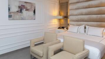 Habitación de hotel con cama, dos sillones, una mesita de noche con lámpara y un cuadro abstracto grande en la pared.