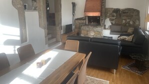 A cozy living room with a stone fireplace, a dining area with a wooden table and chairs, and a black leather sofa. - State-of-the-art within historic walls, a piano of your own, a view of the stork's nest (Neudrossenfeld)