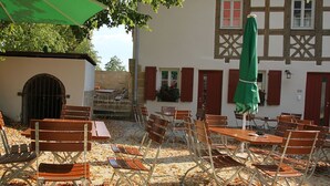 An outdoor seating area with tables and chairs, a green umbrella, and a building with a traditional facade. - State-of-the-art within historic walls, a piano of your own, a view of the stork's nest (Neudrossenfeld)