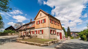 A traditional wooden building with red shutters, a stone foundation, and a clear sky. - State-of-the-art within historic walls, a piano of your own, a view of the stork's nest (Neudrossenfeld)