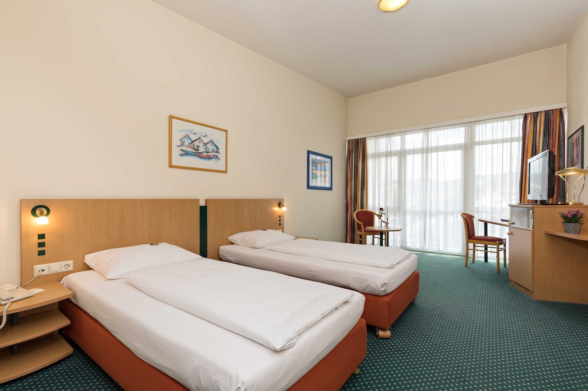 Een hotelkamer met twee bedden, een bureau, een stoel, een televisie en een raam met gordijnen.