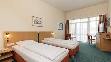 Een hotelkamer met twee bedden, een bureau, een stoel, een televisie en een raam met gordijnen.