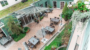 Un espace extérieur aménagé en terrasse, avec des tables et des chaises, entouré de verdure et protégé par une structure en verre.