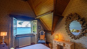 A bedroom with a large bed, a window with a view of the sea, a wooden dresser, and a mirror on the wall.