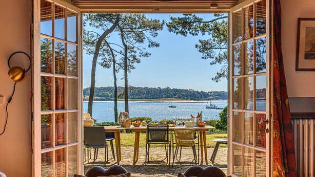 An open door leading to a dining area with a table set for two, overlooking a scenic lake with boats.