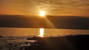 A sunset over a calm sea with a beach in the foreground.