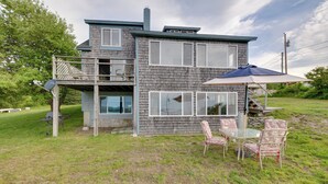 A two-story house with a deck, outdoor seating, and a grill.