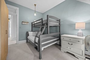 A bunk bed with a headboard, a bedside table with a lamp, and a dresser with drawers.