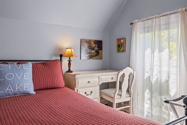 A bedroom with a bed, a desk, a chair, a lamp, and two paintings on the wall.