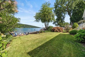 Ein gepflegter Rasen mit einem Steg, einem großen Baum und Blick auf einen See.