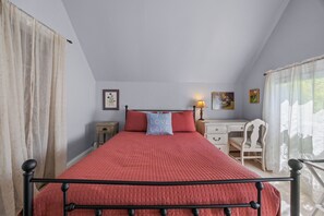 A bedroom with a bed, a desk, a chair, and a window with curtains.