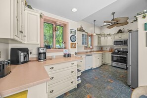 A kitchen with white cabinets, a coffee maker, a microwave, a stove, and a ceiling fan.