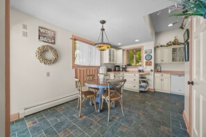 A kitchen with a dining table, chairs, a chandelier, and a window with curtains.