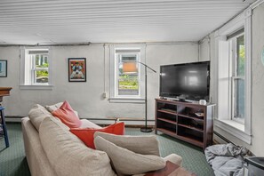 A living room with a beige sofa, red cushions, a television on a wooden stand, and a floor lamp.