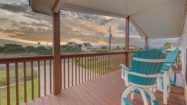 Une terrasse extérieure couverte, dotée de rampes en bois et de fauteuils Adirondack turquoise.