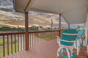 Une terrasse extérieure couverte, dotée de rampes en bois et de fauteuils Adirondack turquoise.