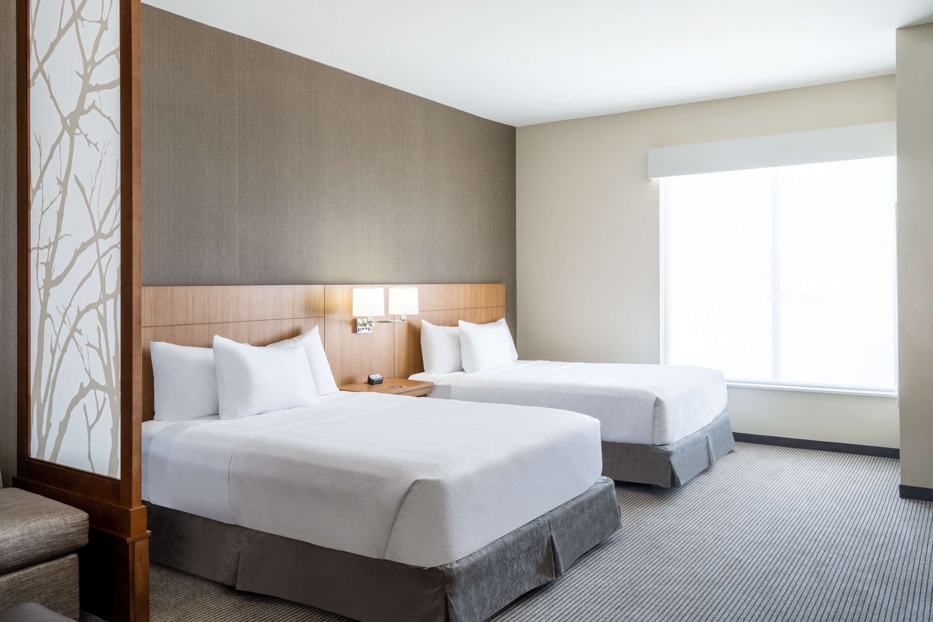A hotel room with two beds, a large window, and a wooden headboard.
