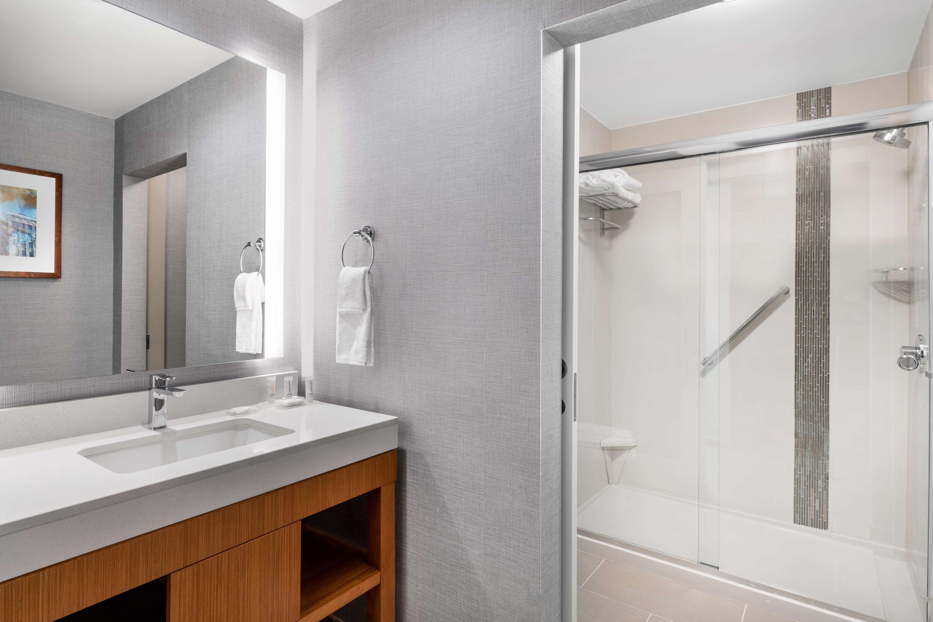 A modern bathroom with a large mirror, two sinks, a wooden vanity, and a glass-enclosed shower area.