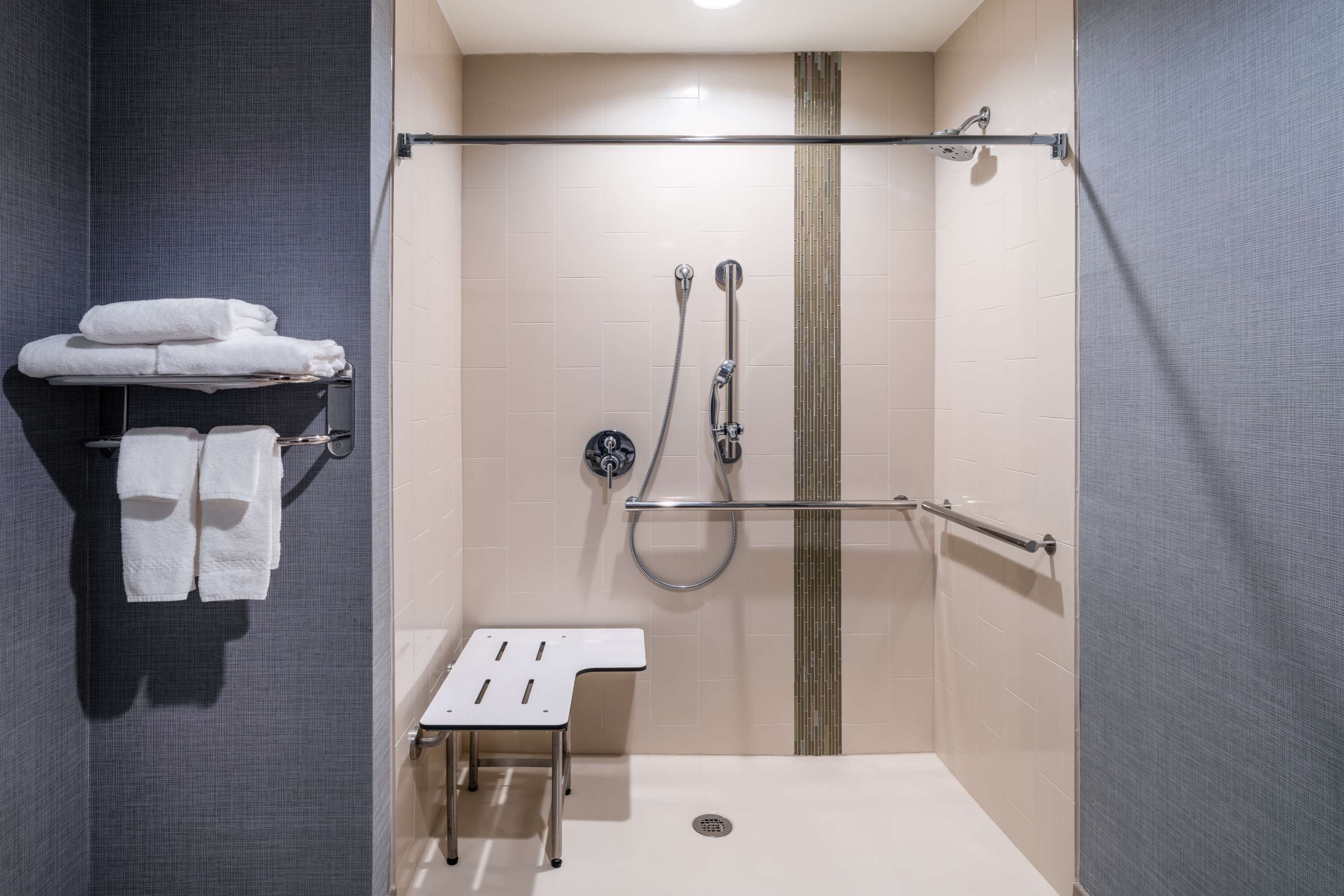 A walk-in shower with a glass door, a towel rack with folded towels, a small table, and a shower control panel.