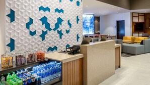 Zona de recepción con un diseño moderno de pared geométrica, una barra con diversos aperitivos y un área de descanso con un sofá amarillo.