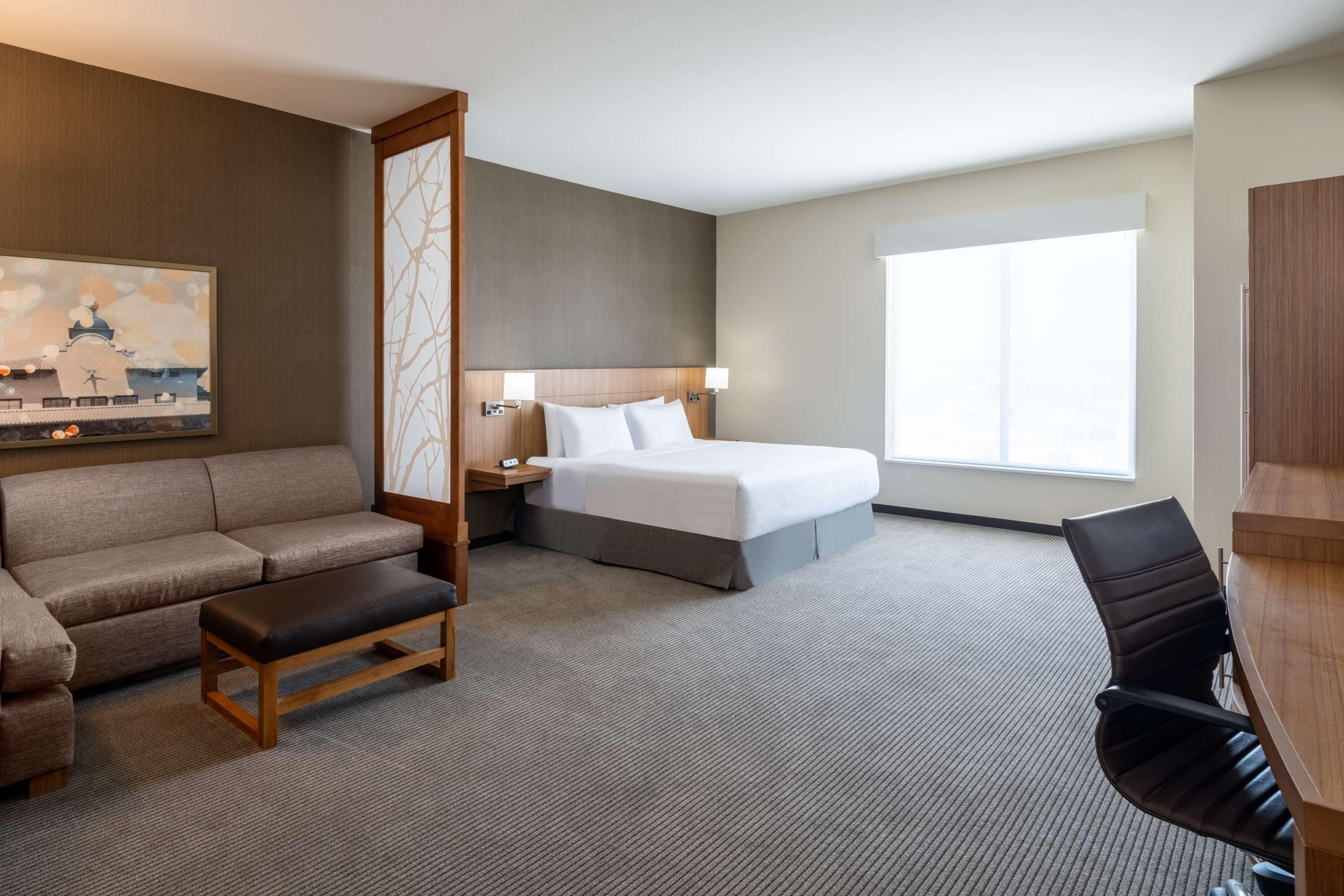 A hotel room with a bed, a sofa, a desk, and a large window.
