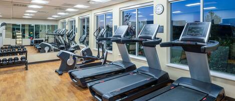 A gym with treadmills, dumbbells, and a clock on the wall.