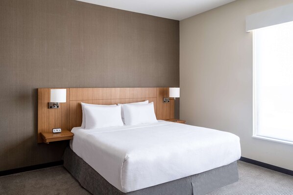 Una habitación de hotel con una cama grande, dos mesitas de noche, una lámpara de pared y una ventana.