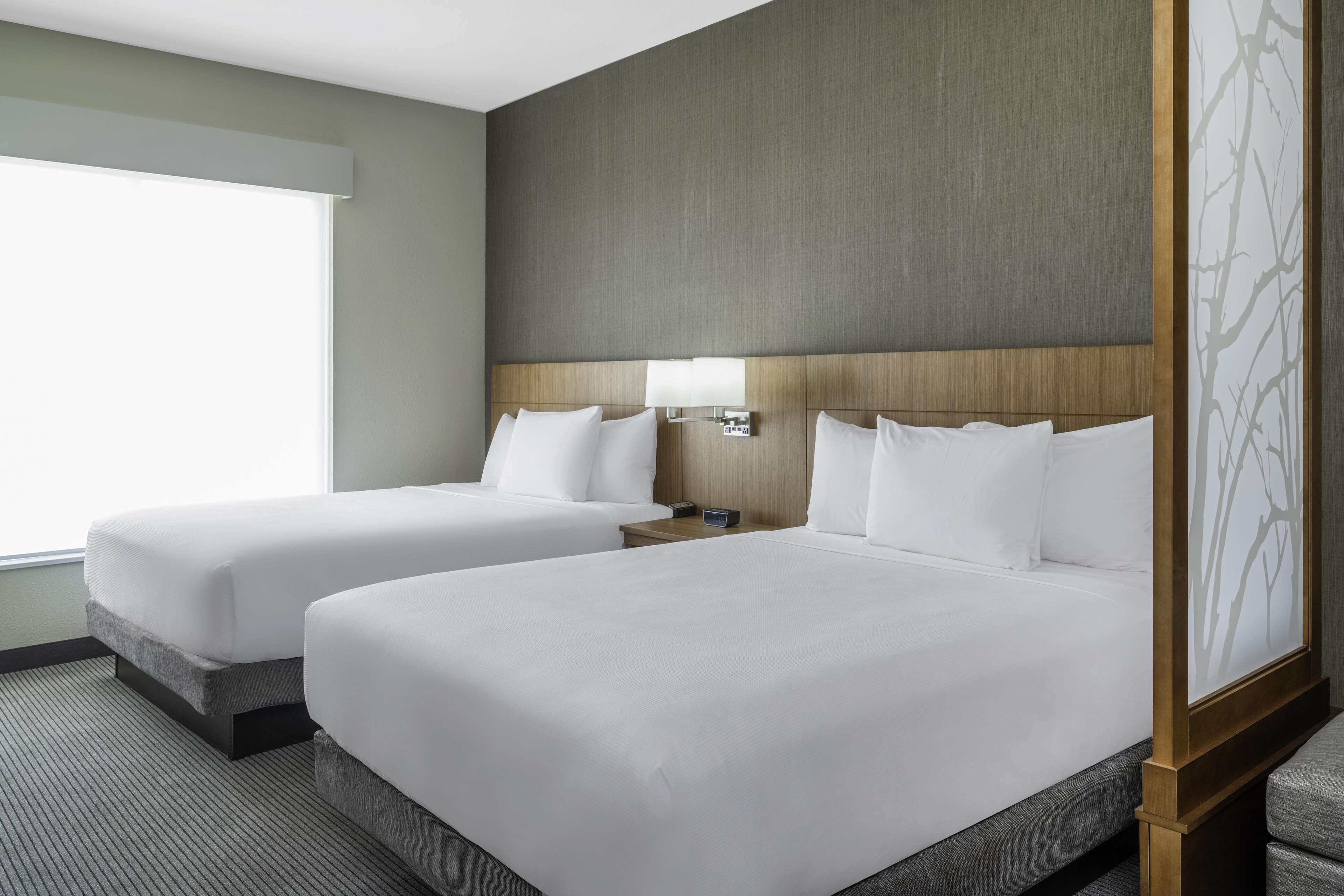 A hotel room with two beds, a nightstand, a lamp, and a window.