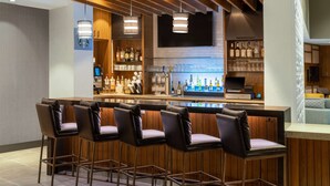 Una zona de bar con taburetes de madera, una barra con exhibición de bebidas y un televisor colgado en la pared.