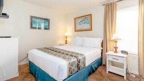 Una habitación de hotel con una cama, lámparas de noche, una mesita de noche, un escritorio y una ventana con cortinas.