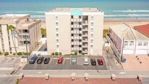 Un hotel con vistas a la playa y al océano. Tiene varios pisos con balcones y un estacionamiento enfrente.