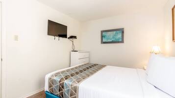 A bedroom with a bed, a TV mounted on the wall, a small dresser, and a painting.