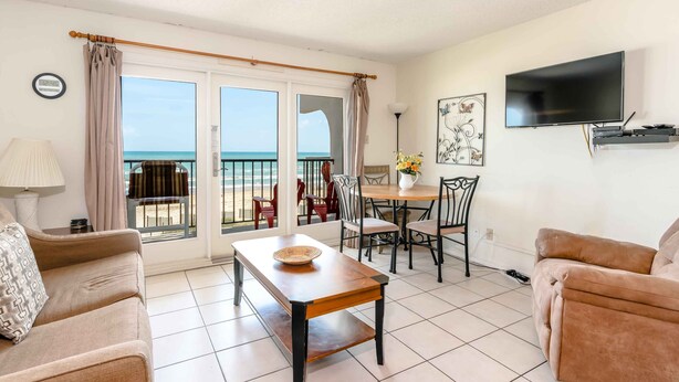 Sala de estar con sofá, una mesa, televisor y vista al mar a través de amplias ventanas.