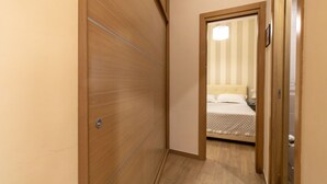 A narrow hallway leading to a bedroom with a bed, a nightstand, and a bedside table.