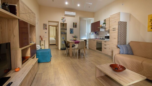 A modern living room with a TV, wooden furniture, a dining area, and a kitchen.