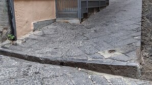 A stone-paved street leading to a building with a metal railing and a small porch.