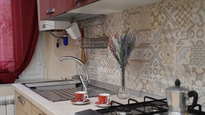 A kitchen with a gas stove, two red cups on the counter, a vase with flowers, and patterned tiles on the wall.