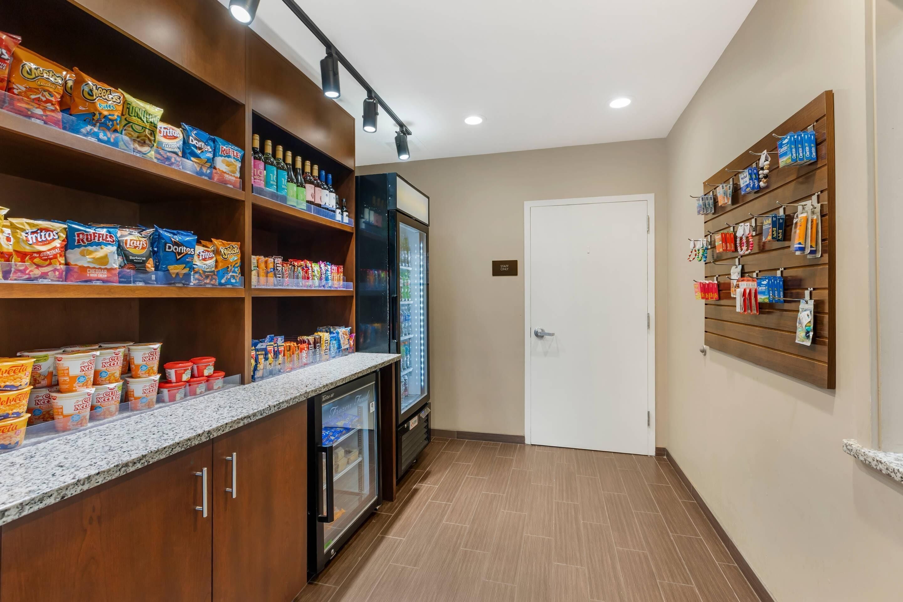 A hotel pantry with shelves stocked with snacks, a refrigerator, and a door.