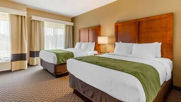 A hotel room with two beds, a large window with curtains, a wooden headboard, and a carpeted floor.