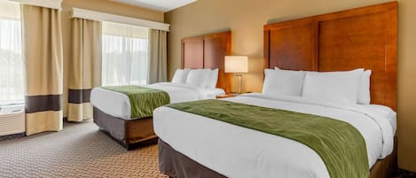 A hotel room with two beds, a large window with curtains, a wooden headboard, and a carpeted floor.