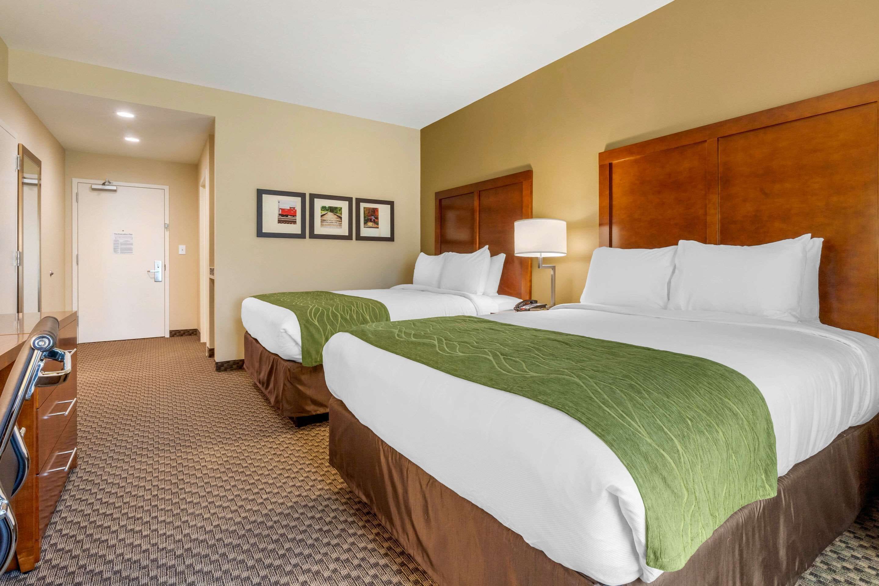 Een hotelkamer met twee bedden, een houten hoofdeinde, een vloerbedekking en een deur naar een andere kamer.