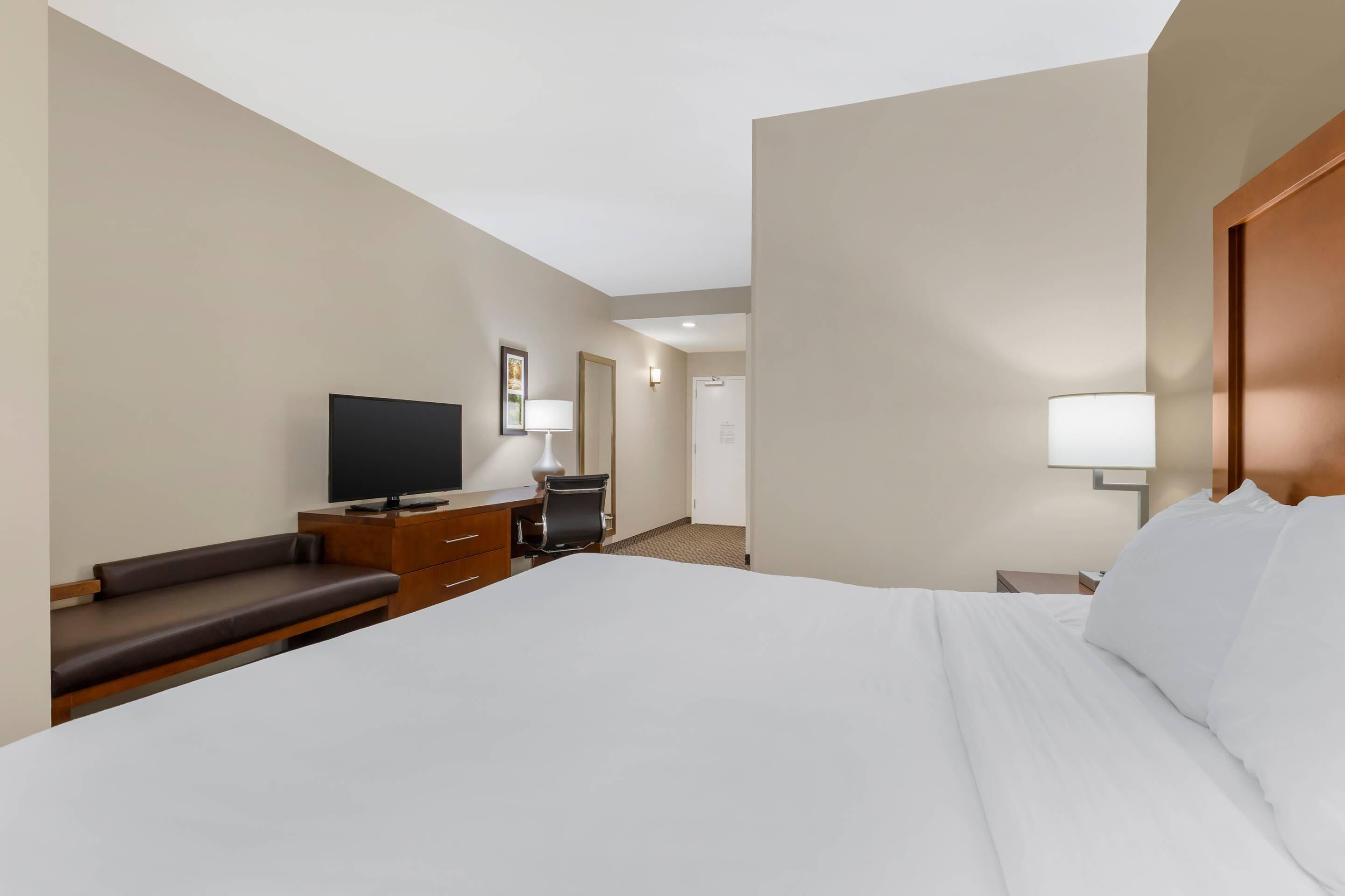 A hotel room with a large bed, a desk with a chair, a television, and a lamp.
