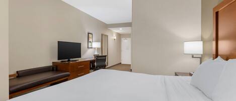 A hotel room with a large bed, a desk with a chair, a television, and a lamp.